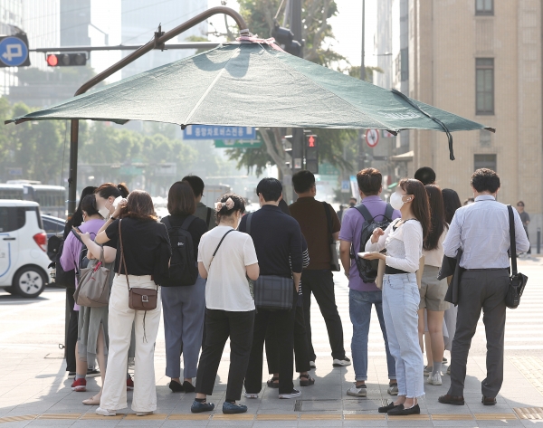 서울 광화문역 인근에서 출근하는 시민들이 그늘막 밑에서 햇빛을 피하며 신호를 기다리고 있다.